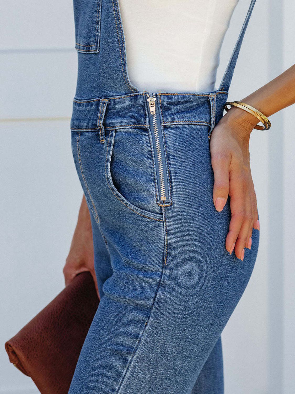 Close-up side view of Prairie Belle raw hem denim overalls featuring side zipper detail and flared leg western style denim.